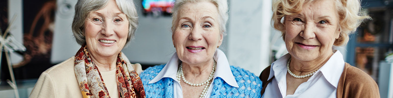 Three independent living female residents standing together smiling with their arms around each other